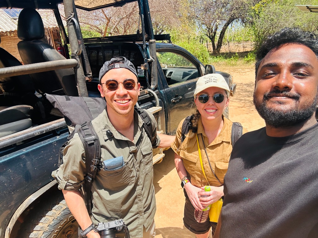 Malindu and safari guests smiling beside their safari jeep